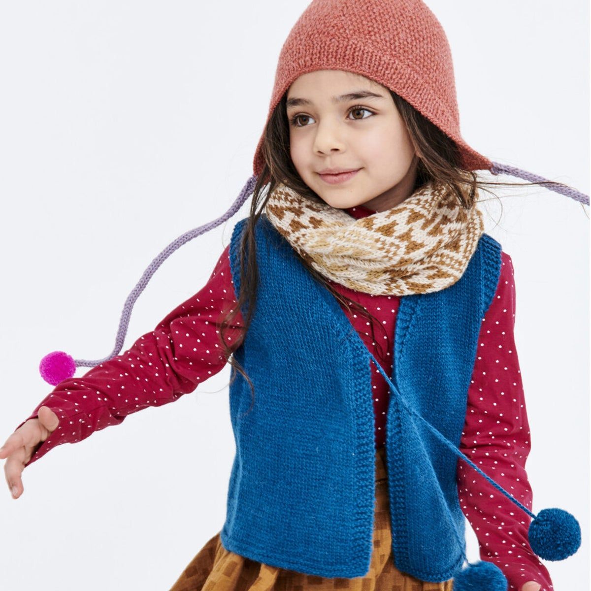 A little girl in a knit scarf, hat and vest