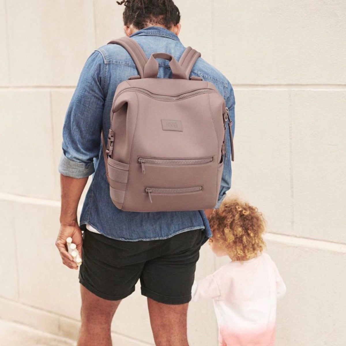 A man wearing a back-pack and holding a child's hand