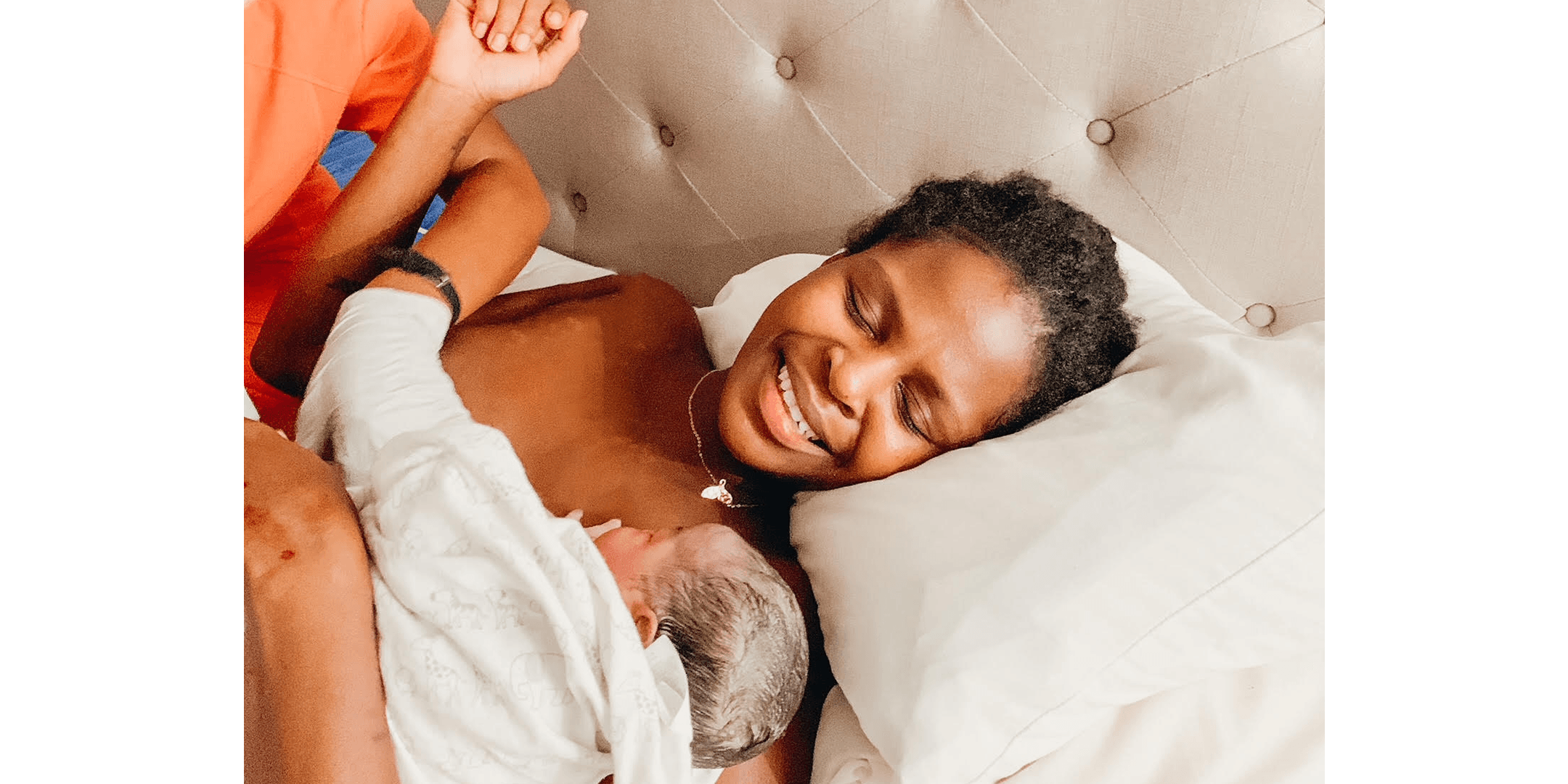 Geena Whyte smiling and holding her newborn baby Olena wrapped in a blanket.