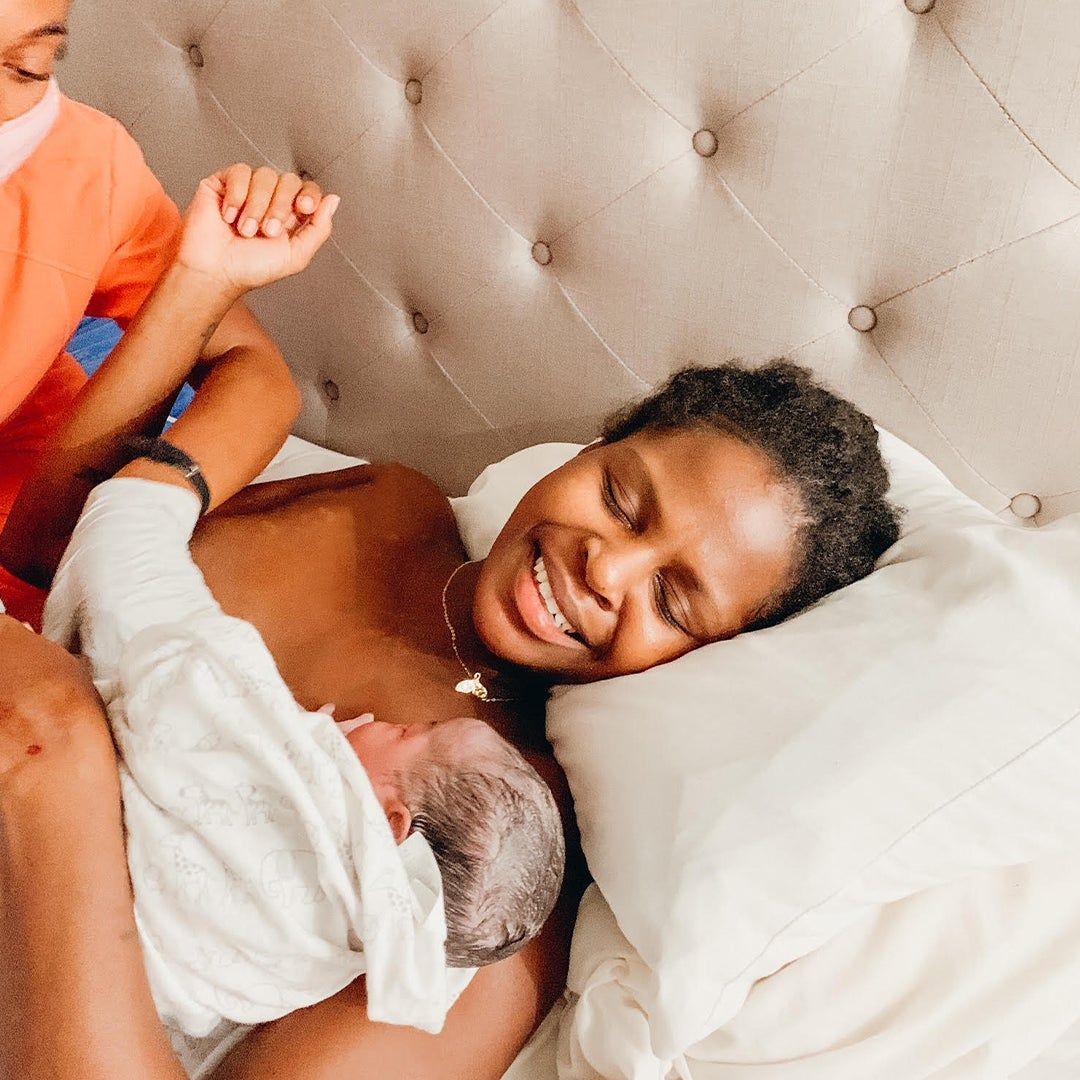 Geena Whyte smiling and holding her newborn baby Olena wrapped in a blanket.