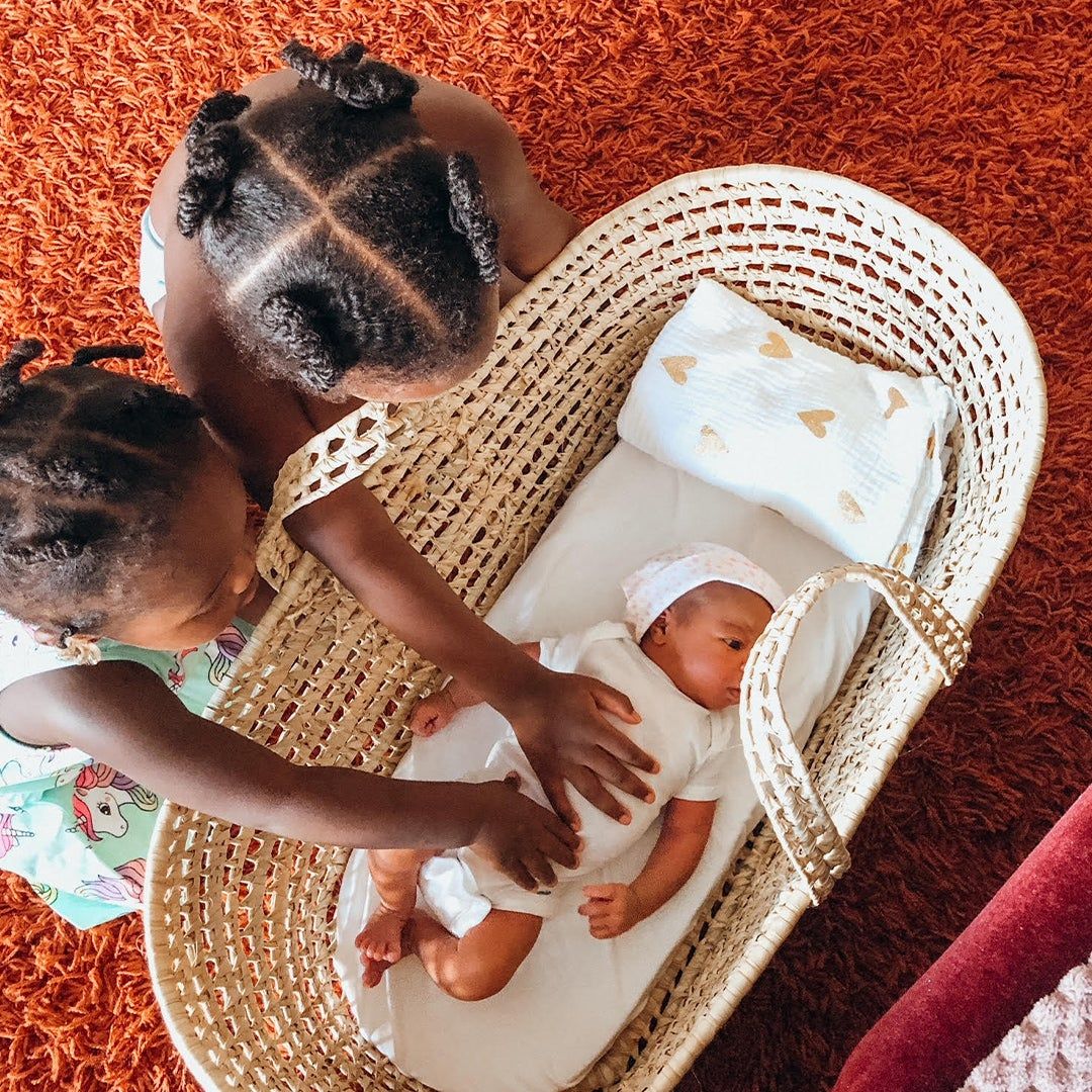 Geena Whyte's daughters Paloma and Amaris with their hands on their newborn baby sister Olena laying in a basket.