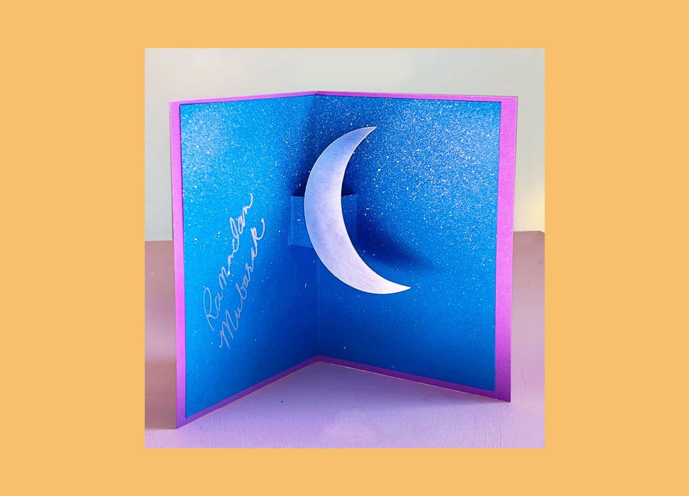 Picture of an open blue card craft for kids with a moon inside for Ramadan.