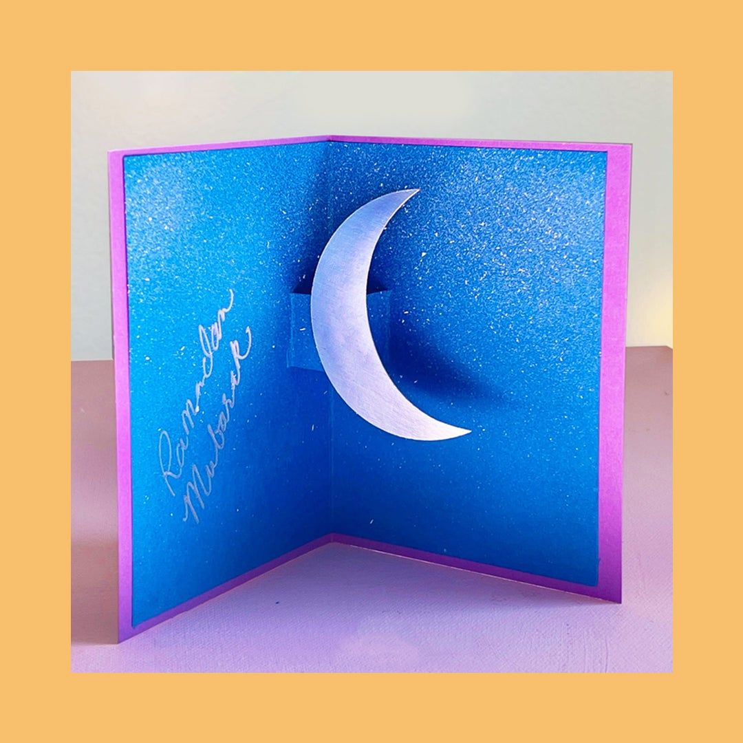 Picture of an open blue card craft for kids with a moon inside for Ramadan.