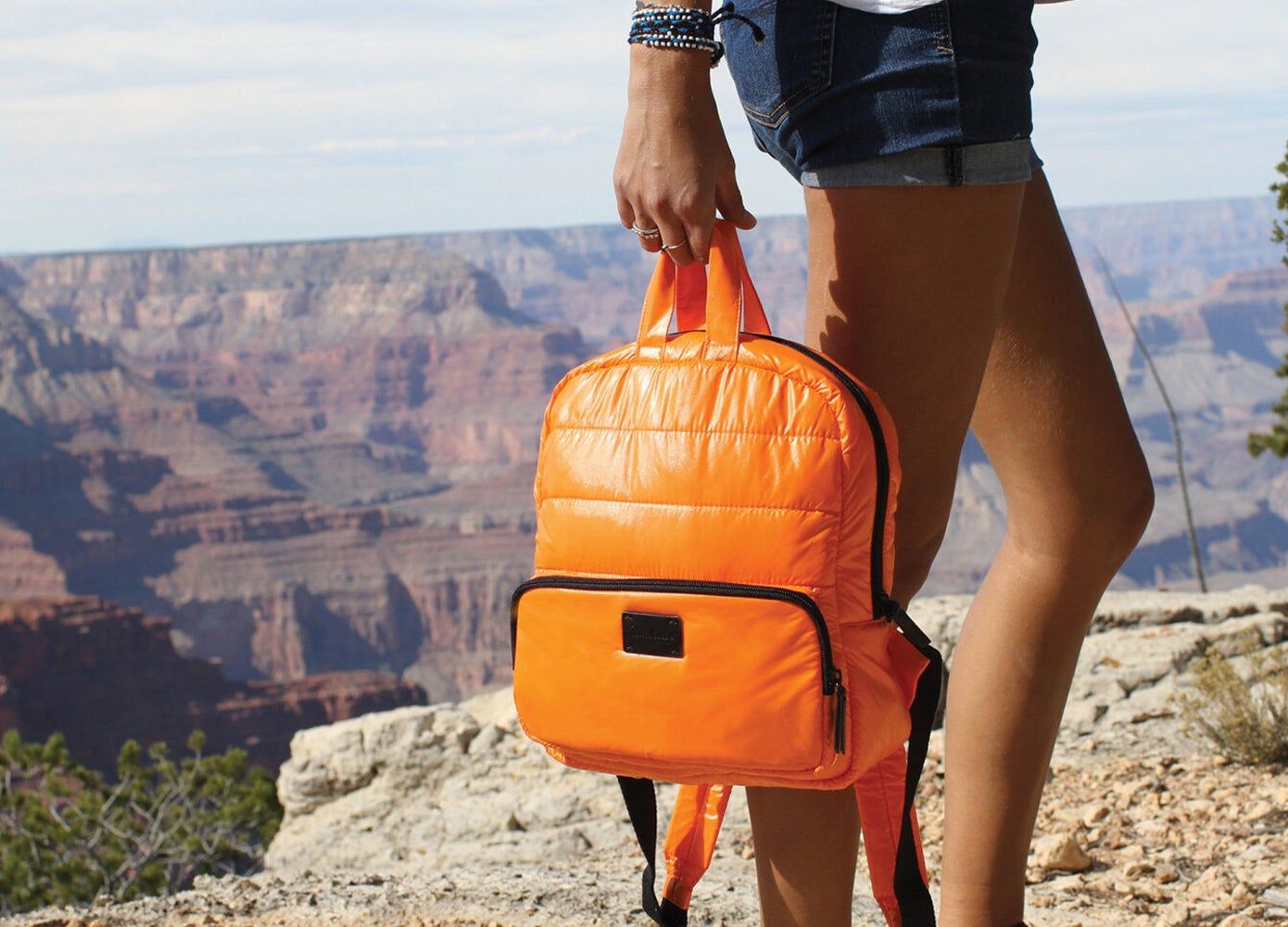 Woman holding a bright orange backpack standing by a canyon