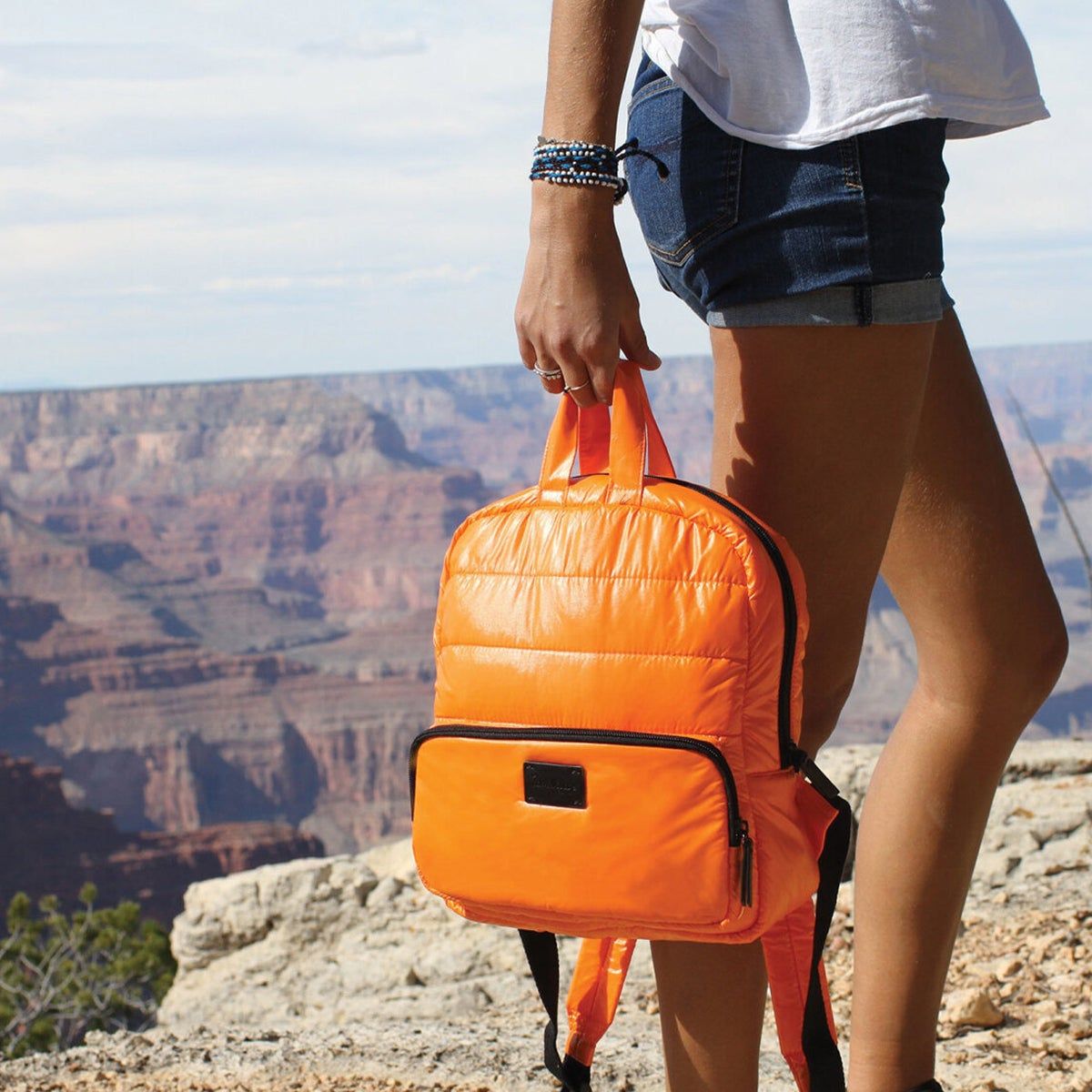 Woman holding a bright orange backpack standing by a canyon
