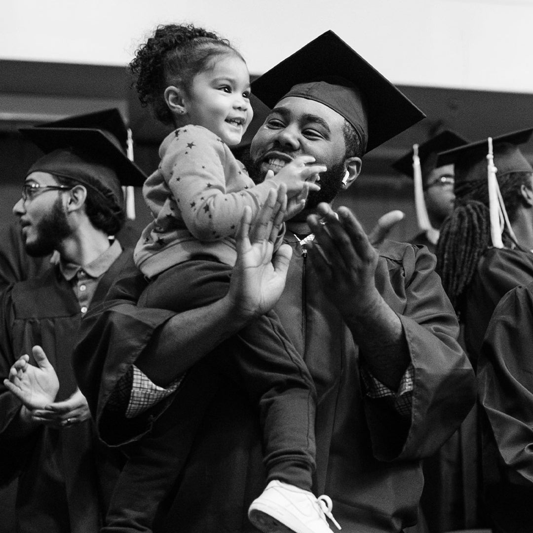 image of a father at his graduation ceremony holding his smiling daughter