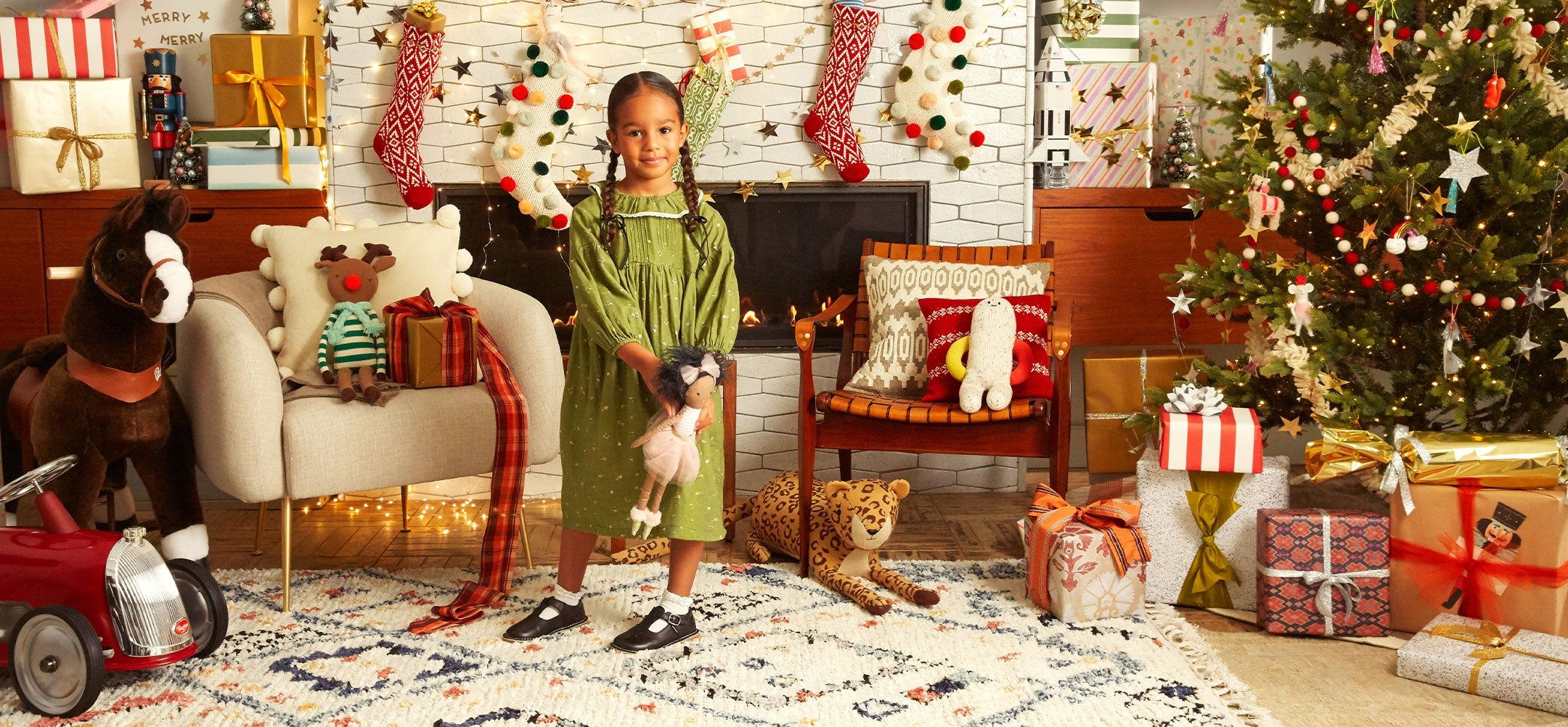 photo of a young girl dressed in a festive green dress. She is standing in a living room decorated with holiday decor and a christmas tree and surrounded by presents.