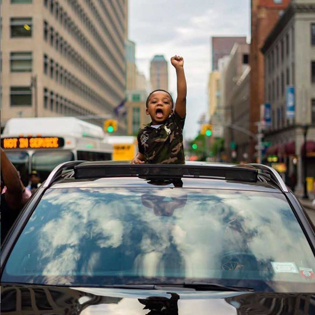 child standing out of a sun roof raising their fist