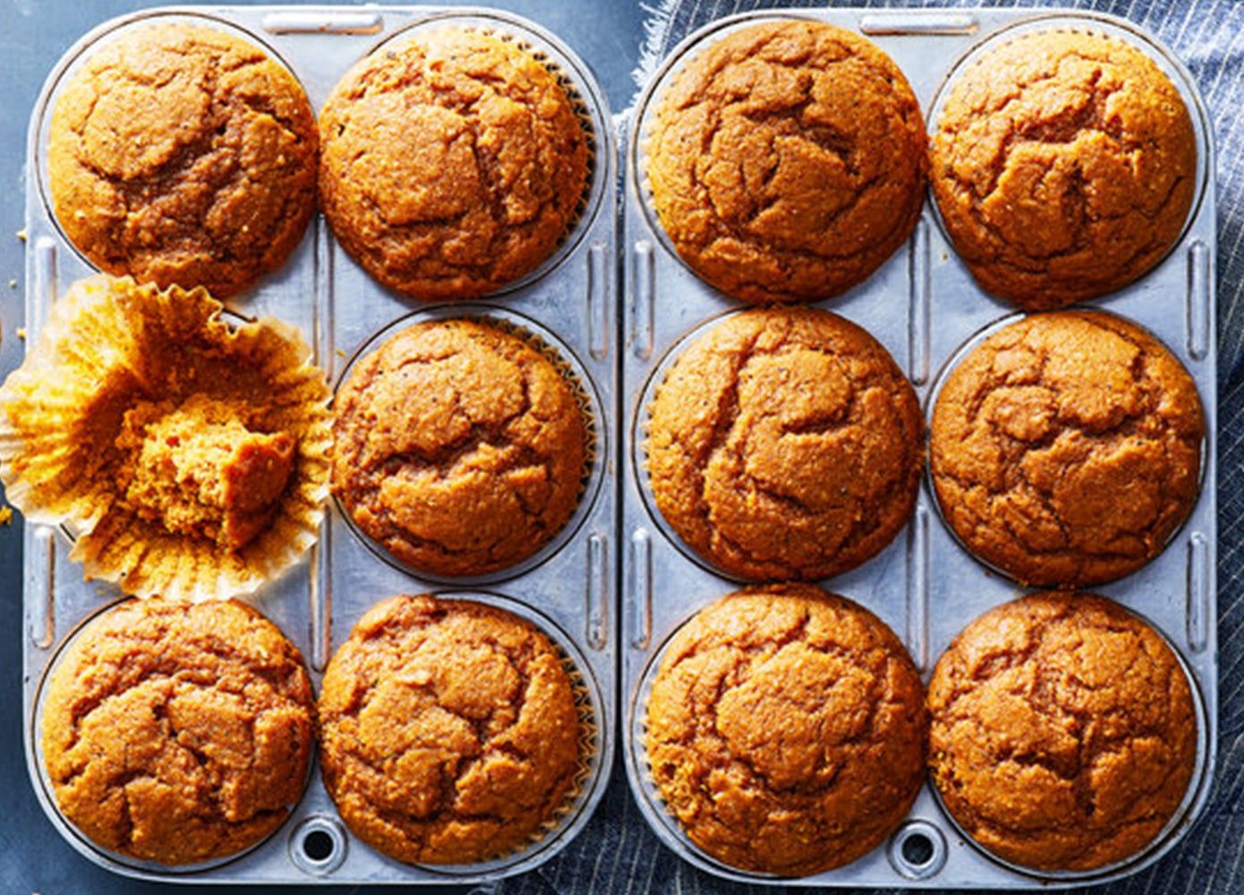 Two trays of six baked pumpkin muffins with one muffin half-eaten
