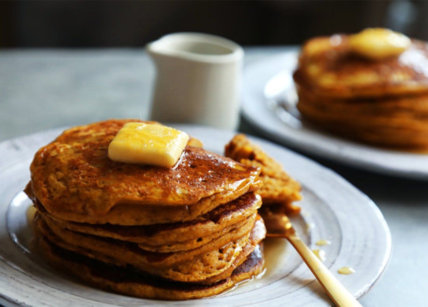 Two plates of stacked pumpkin pancakes with butter and syrup