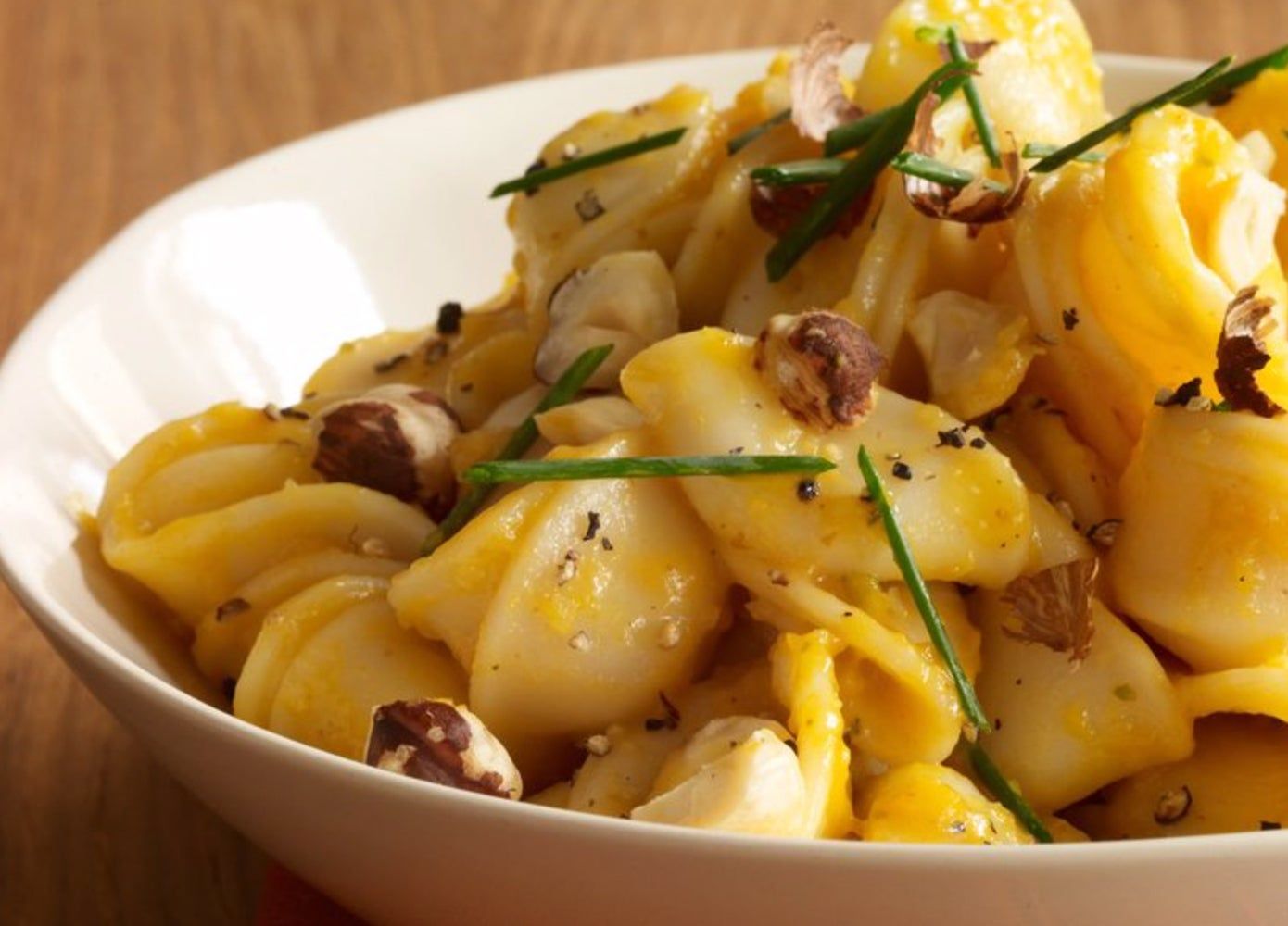 Close photo of a bowl of cooked pumpkin pasta topped with toasted hazelnuts