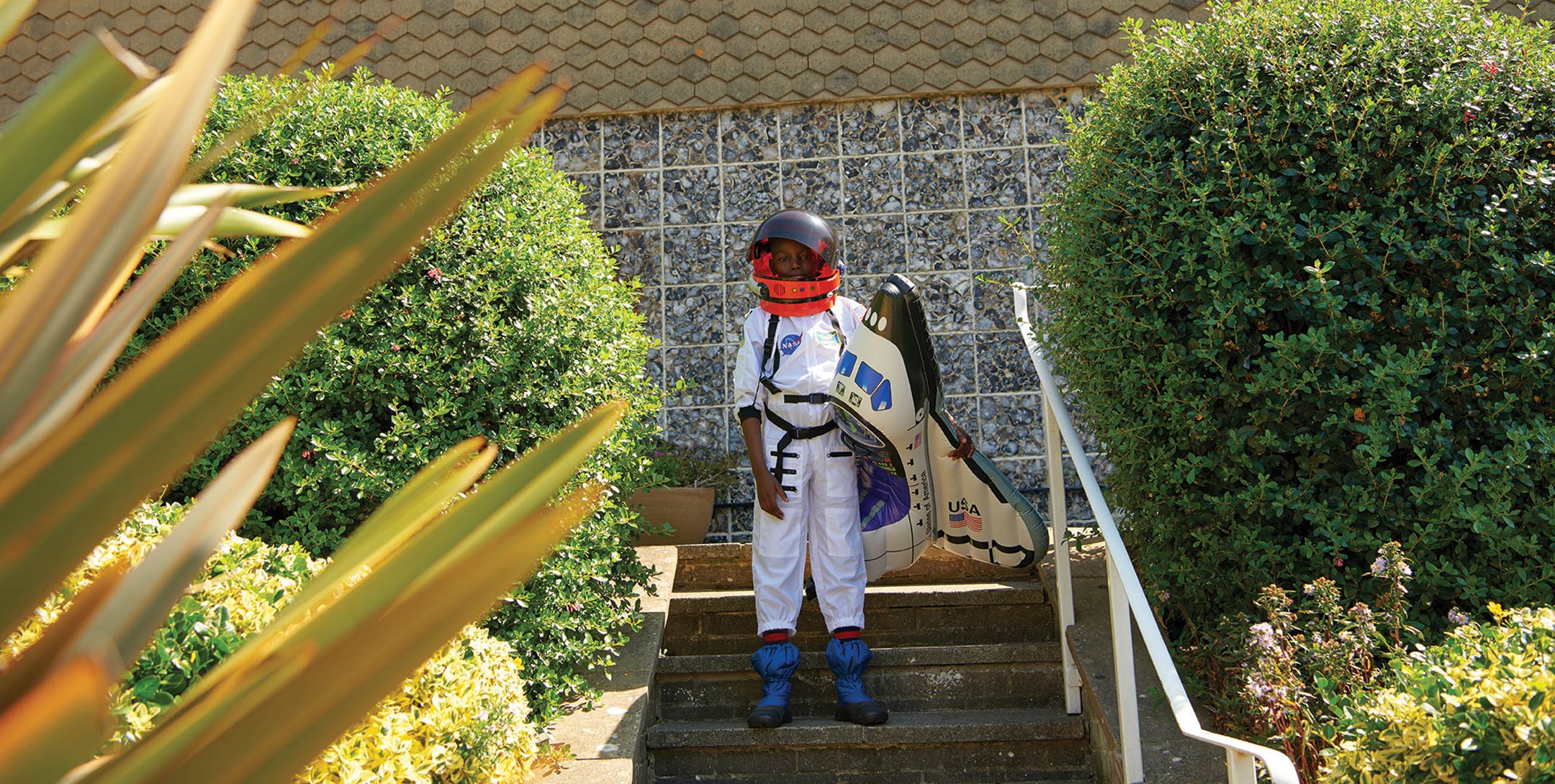 photo of a boy celebrating halloween wearing an astronaut suit and holding an inflatable spaceship