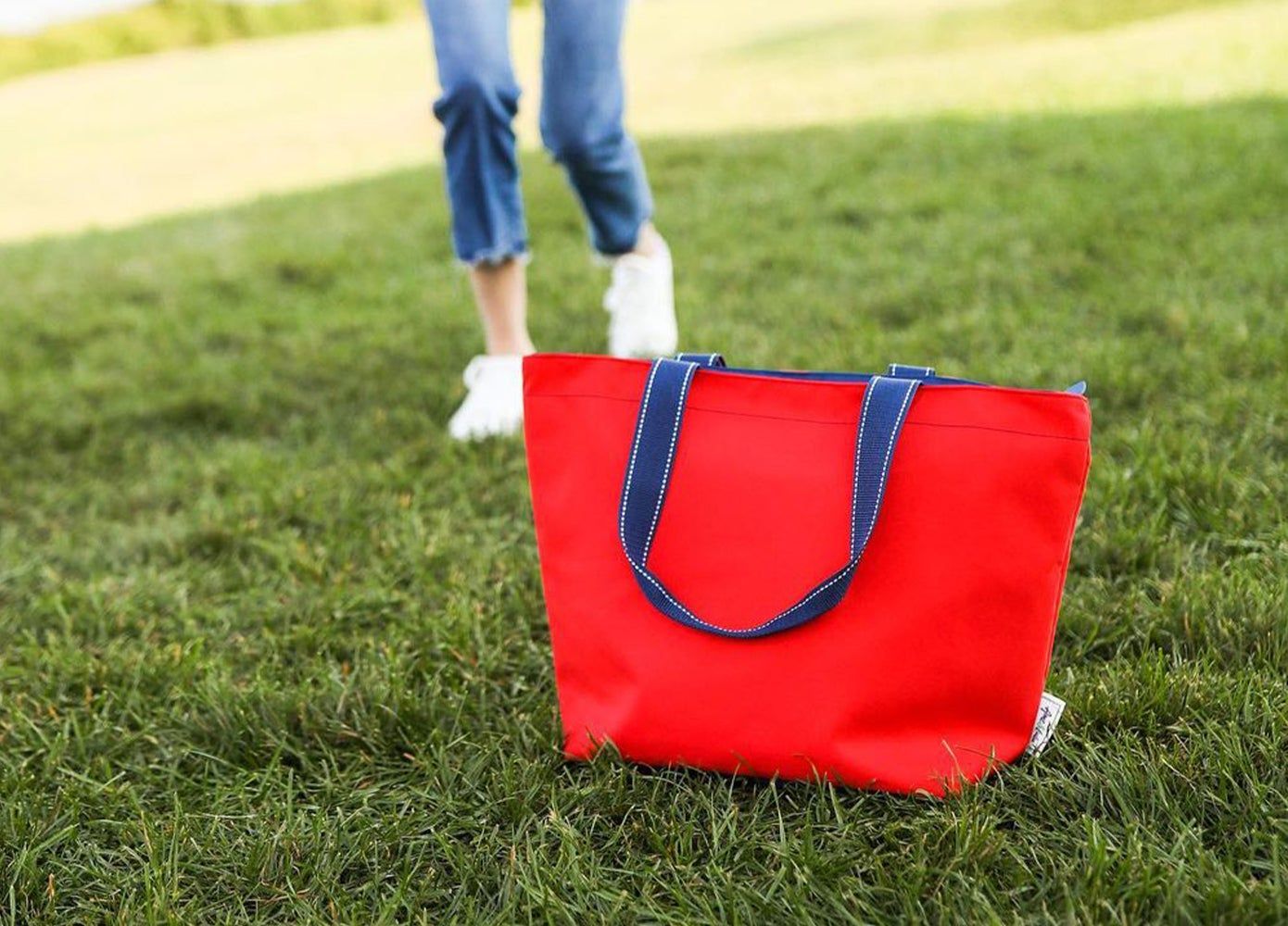 A red tote on green grass with a person in the background