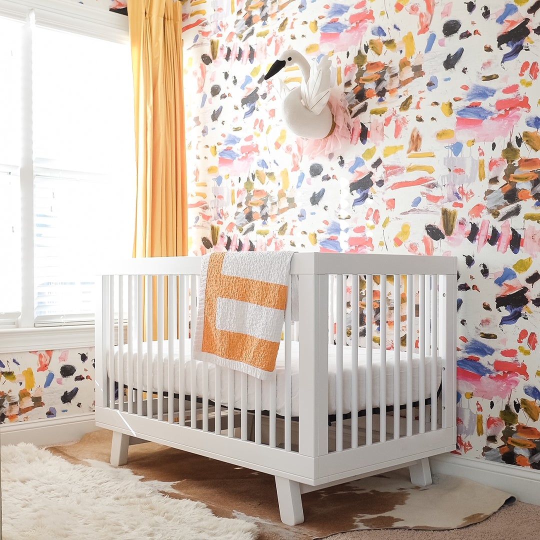 a white crib against a colorful wallpaper wall