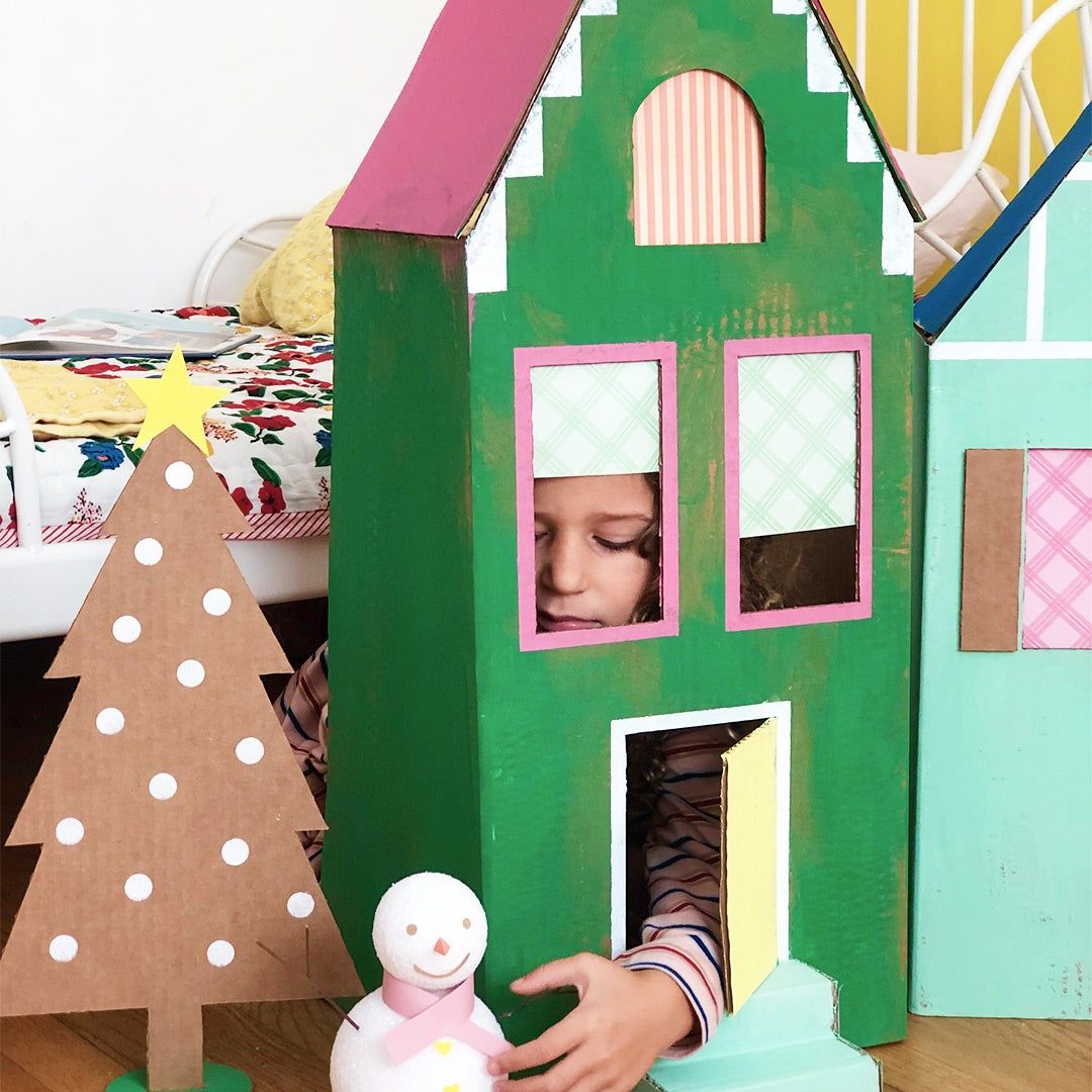 a little girl inside a colorful cardboard box house playing with a snowman