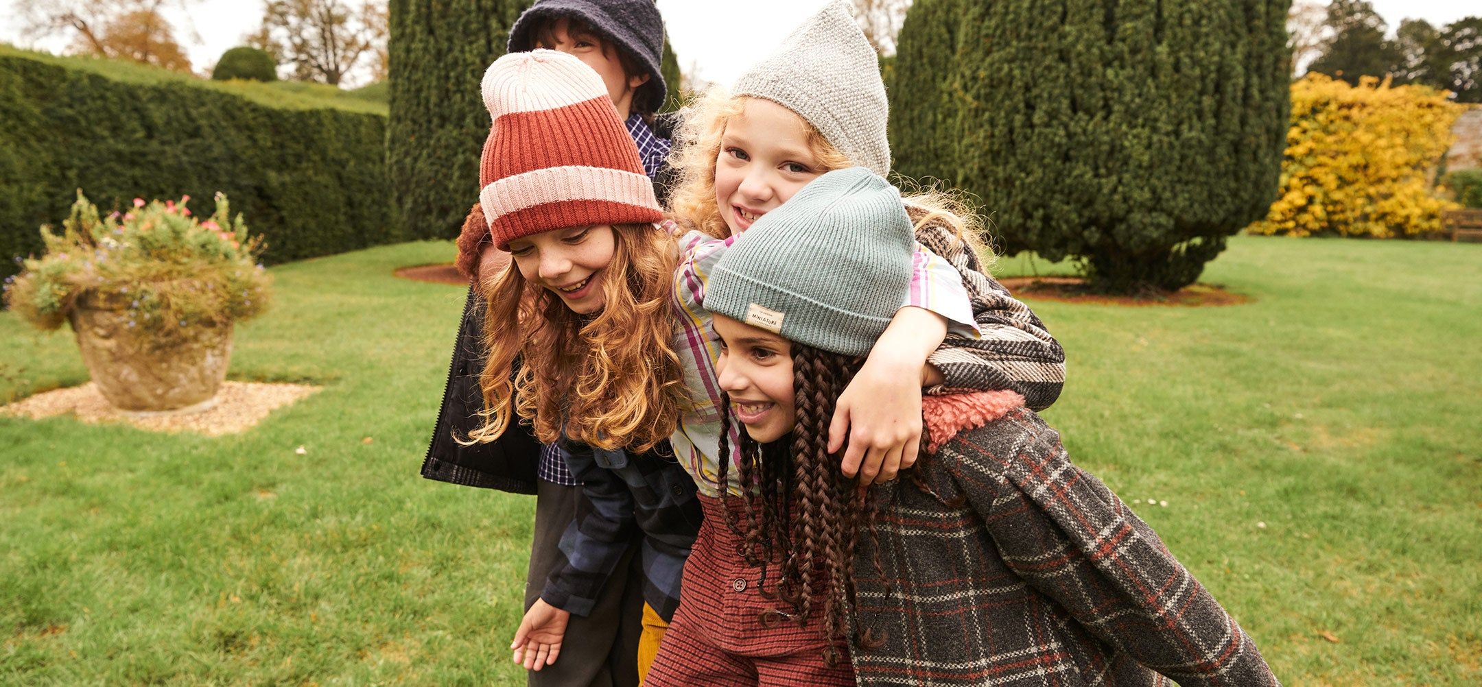 Four children huddled as a group wearing winter hats and plaid