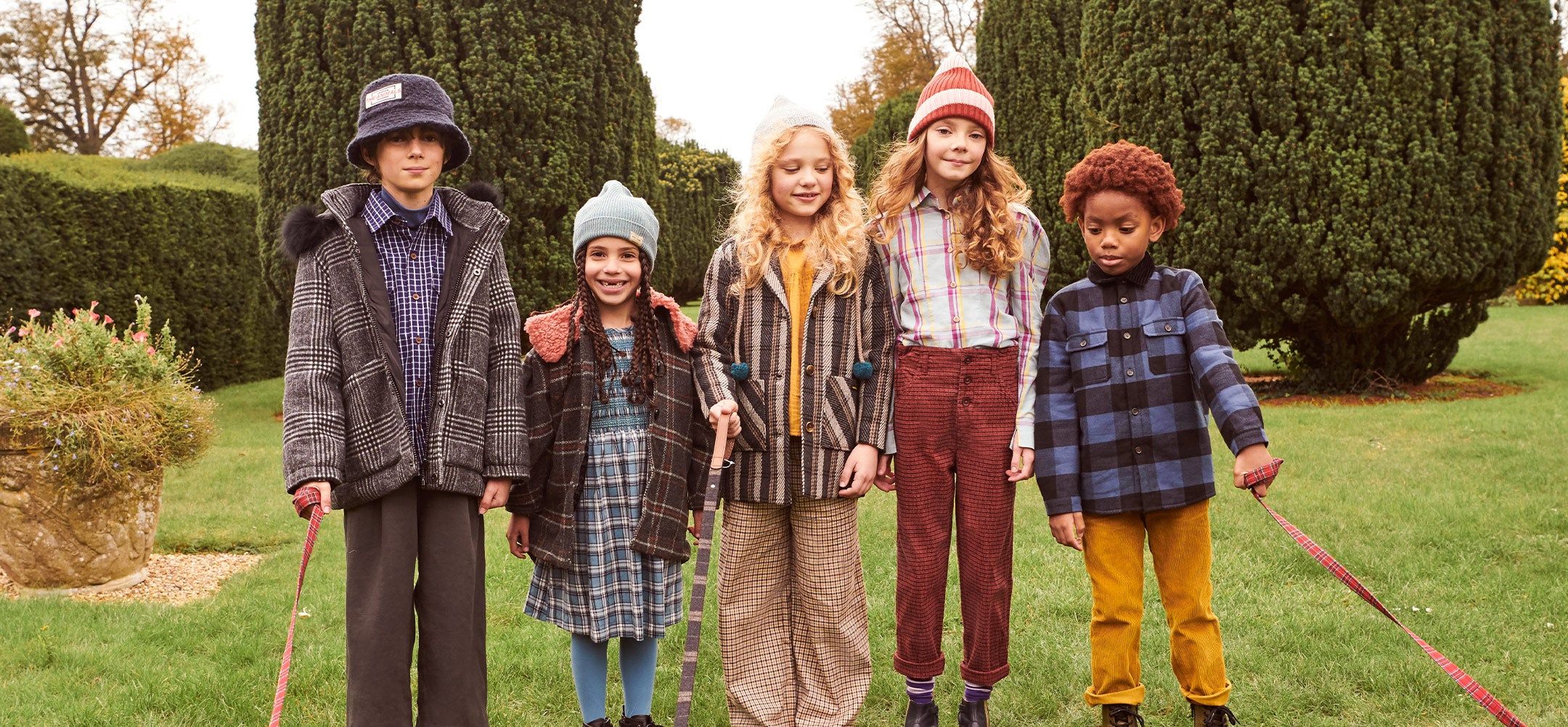 A group of children standing in a garden wearing winter clothes in plaid and tartan