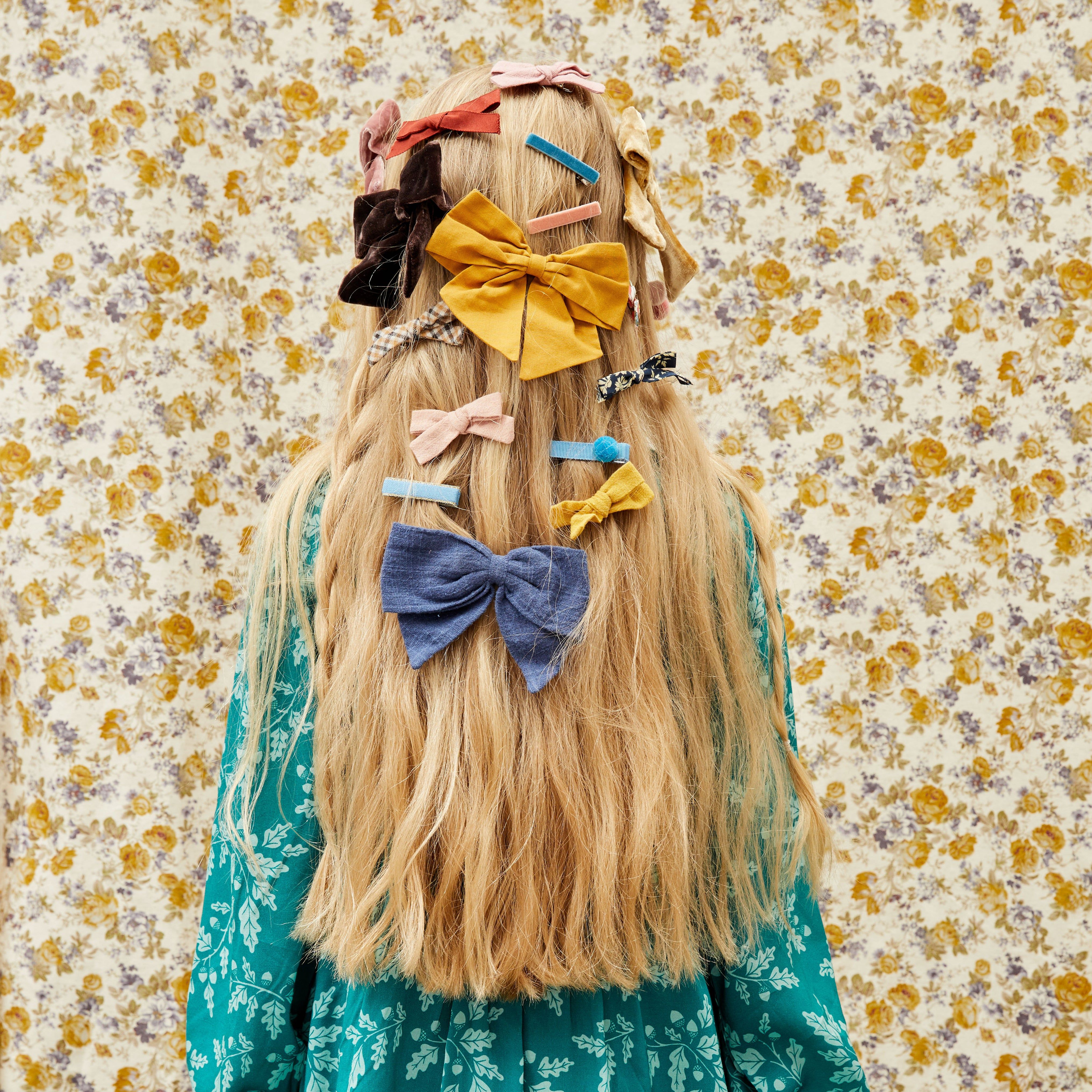 girl with long hair and many hair bows in her hair in front of a patterned backdrop