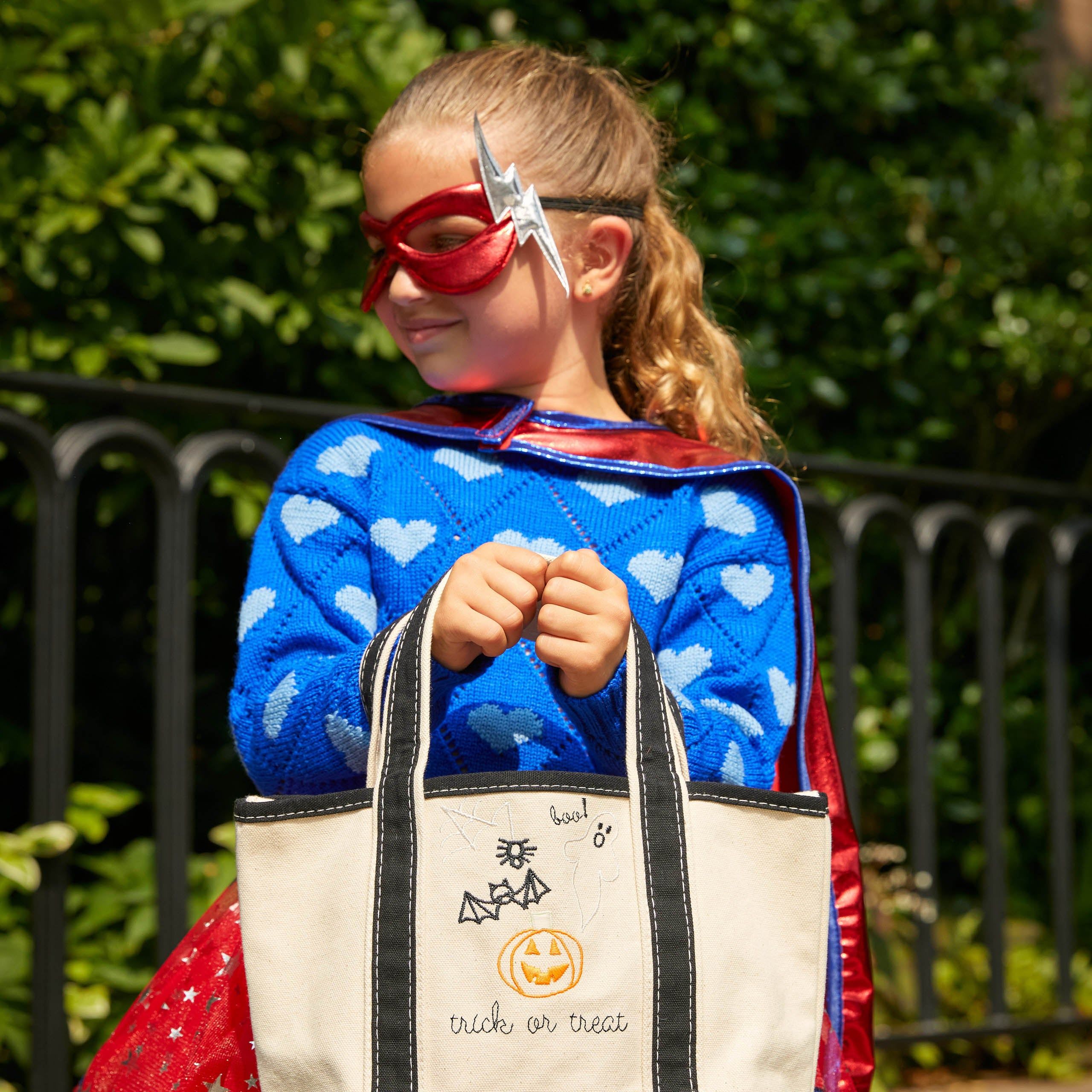 girl dressed in superhero Halloween costume with trick-or-treat bag