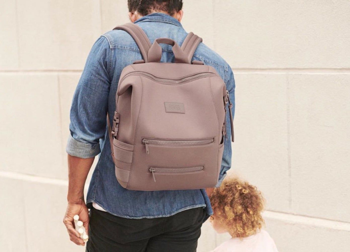 A man wearing a back-pack and holding a child's hand
