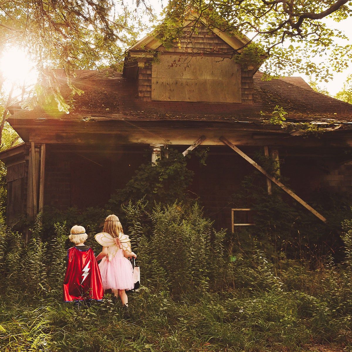 Two children in costumes walking into a scary abandoned house