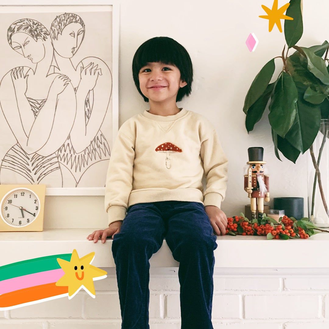 Little boy wearing the mushroom sweatshirt sitting with plants and art