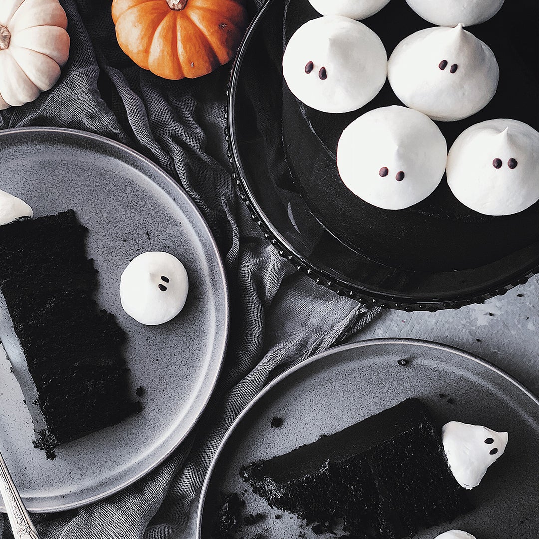 a black cake with black icing topped with ghost meringues