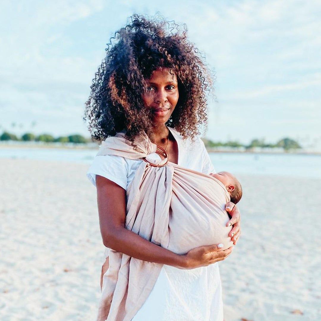 Mother Geena Whyte holding a baby in a wrap on a beach