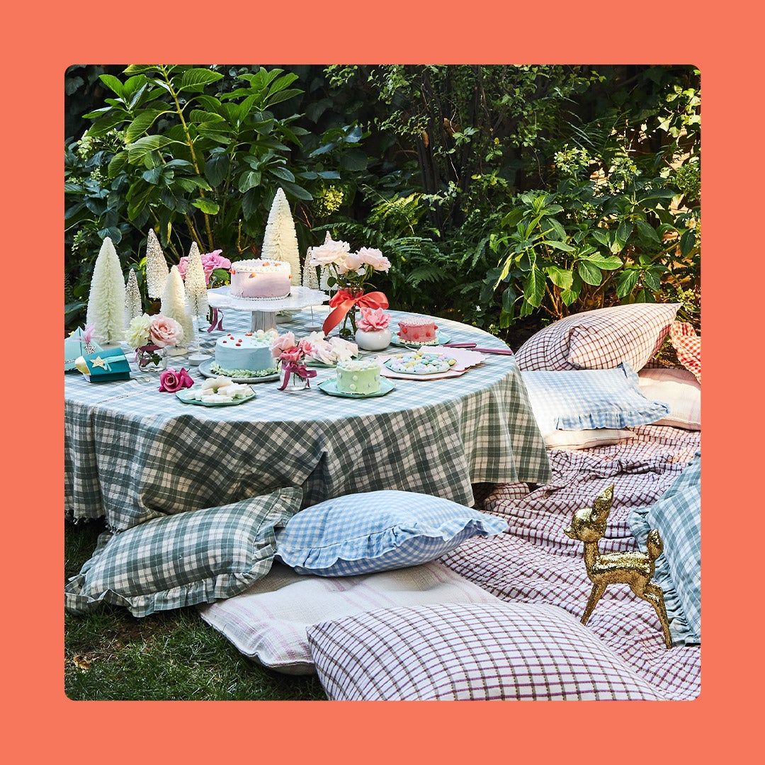 Beautiful outdoor tablescape with plaid linens, flowers, trees, pillows