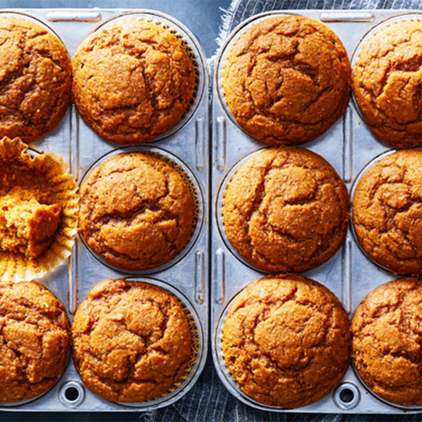 Two trays of six baked pumpkin muffins with one muffin half-eaten