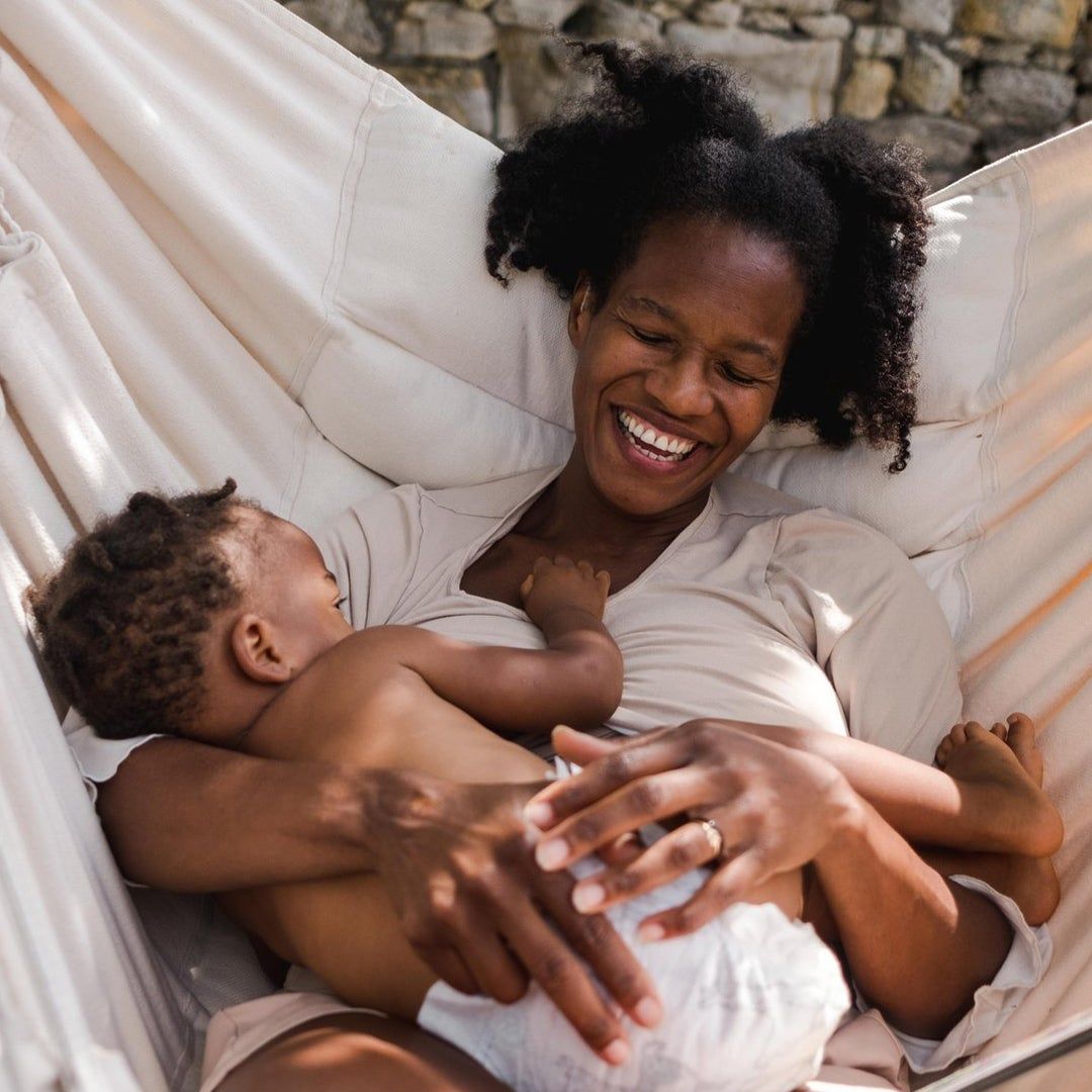 A smiling black woman and baby lounging in a hammock.