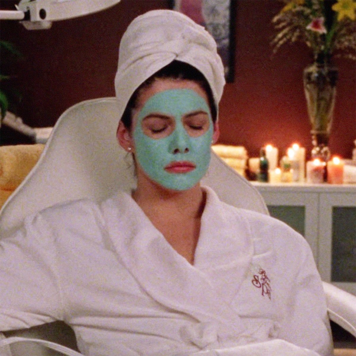 Woman with eyes closed in a spa robe and towel with a green face mask