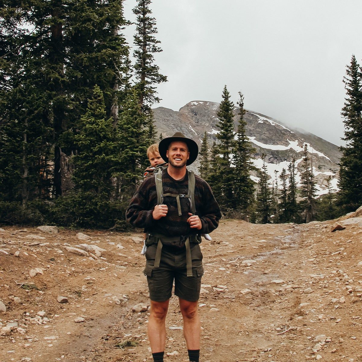 Matthew in front of a mountain with Uma in a hiking pack; Elliot looking over a lake with Uma in a hiking pack