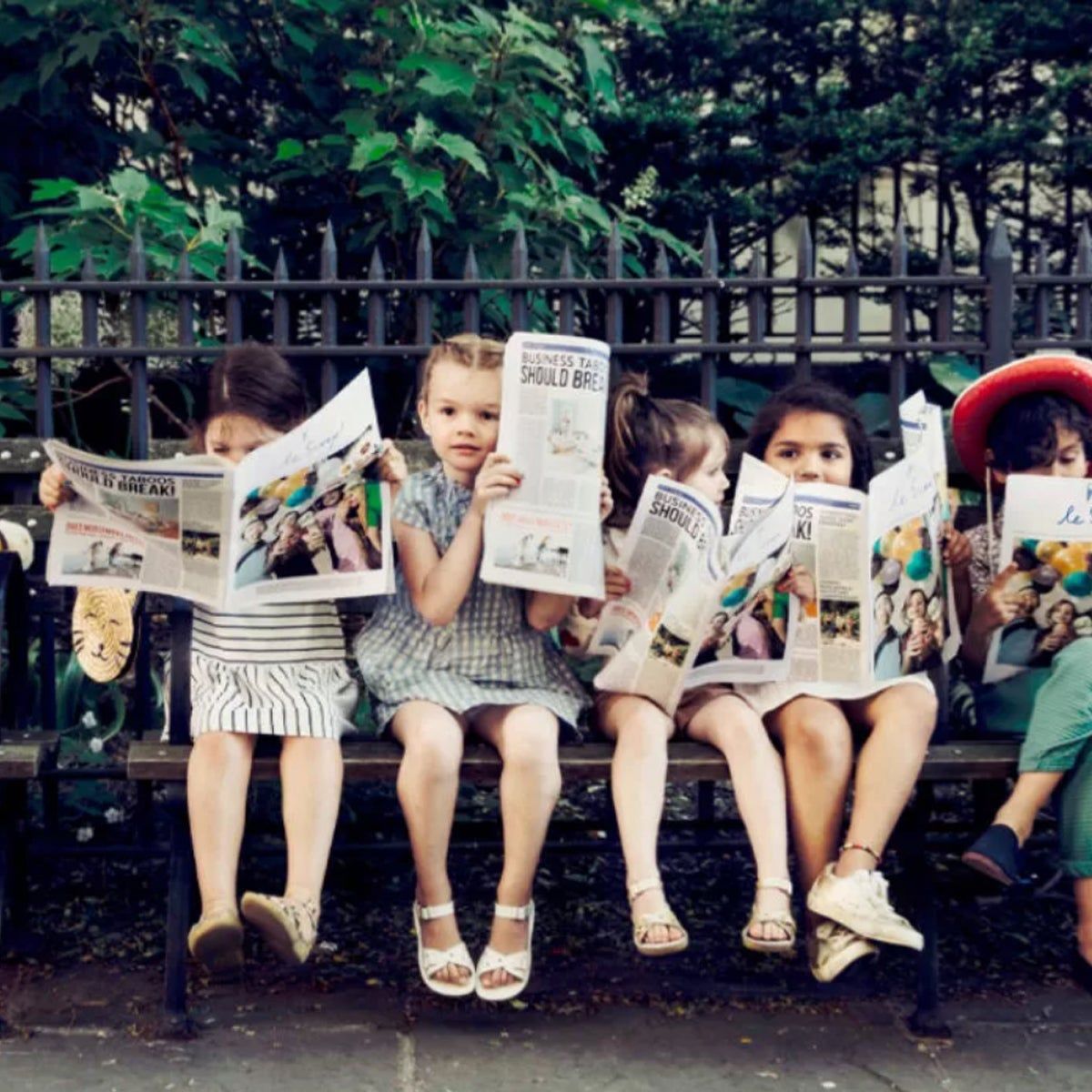 kids sitting on a bench reading the paper