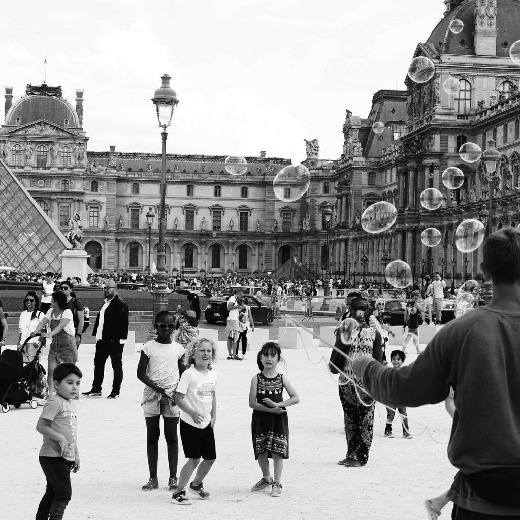 kids playing with bubbles in front the the Louvre in Paris