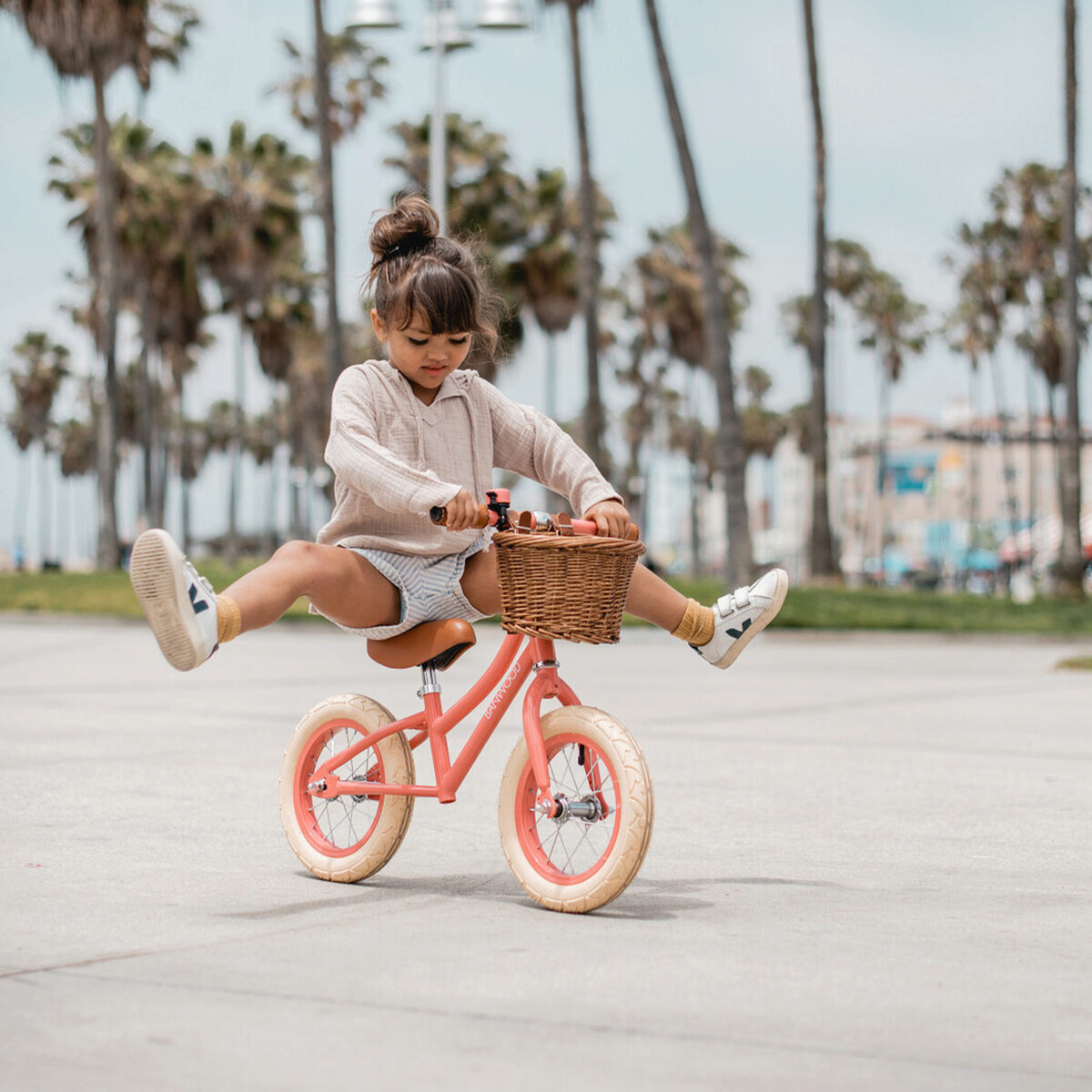A little girl riding a balance bike with palm trees in the background