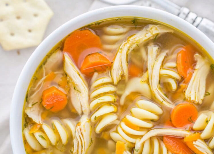 bowl of chicken noodle soup with saltine cracker and spoon