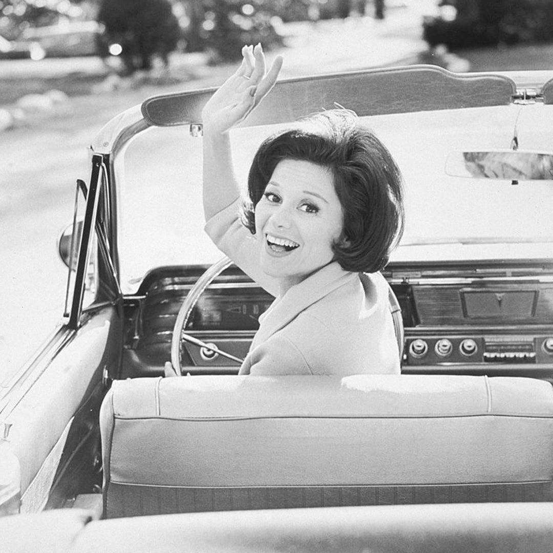 black and white image of a woman in a convertible turning around and waving