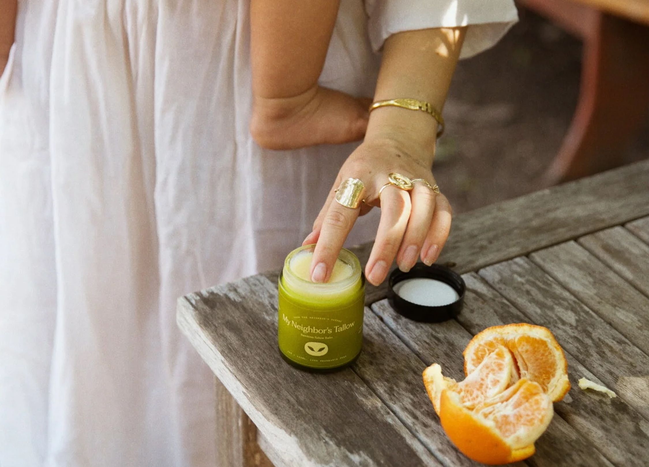 A woman who is baby wearing scoops body balm onto her fingers.