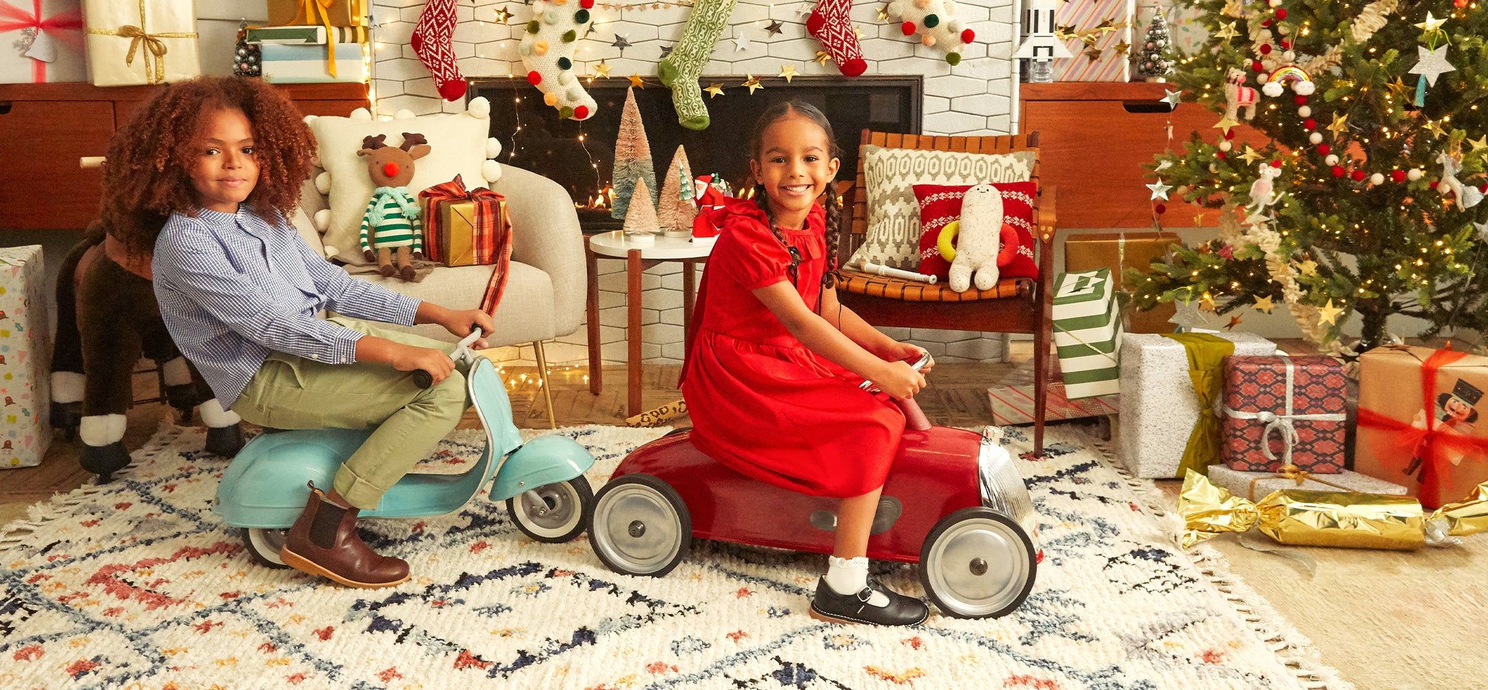 two children in a living room decorated with Christmas gifts and decor and playing with ride-on toys