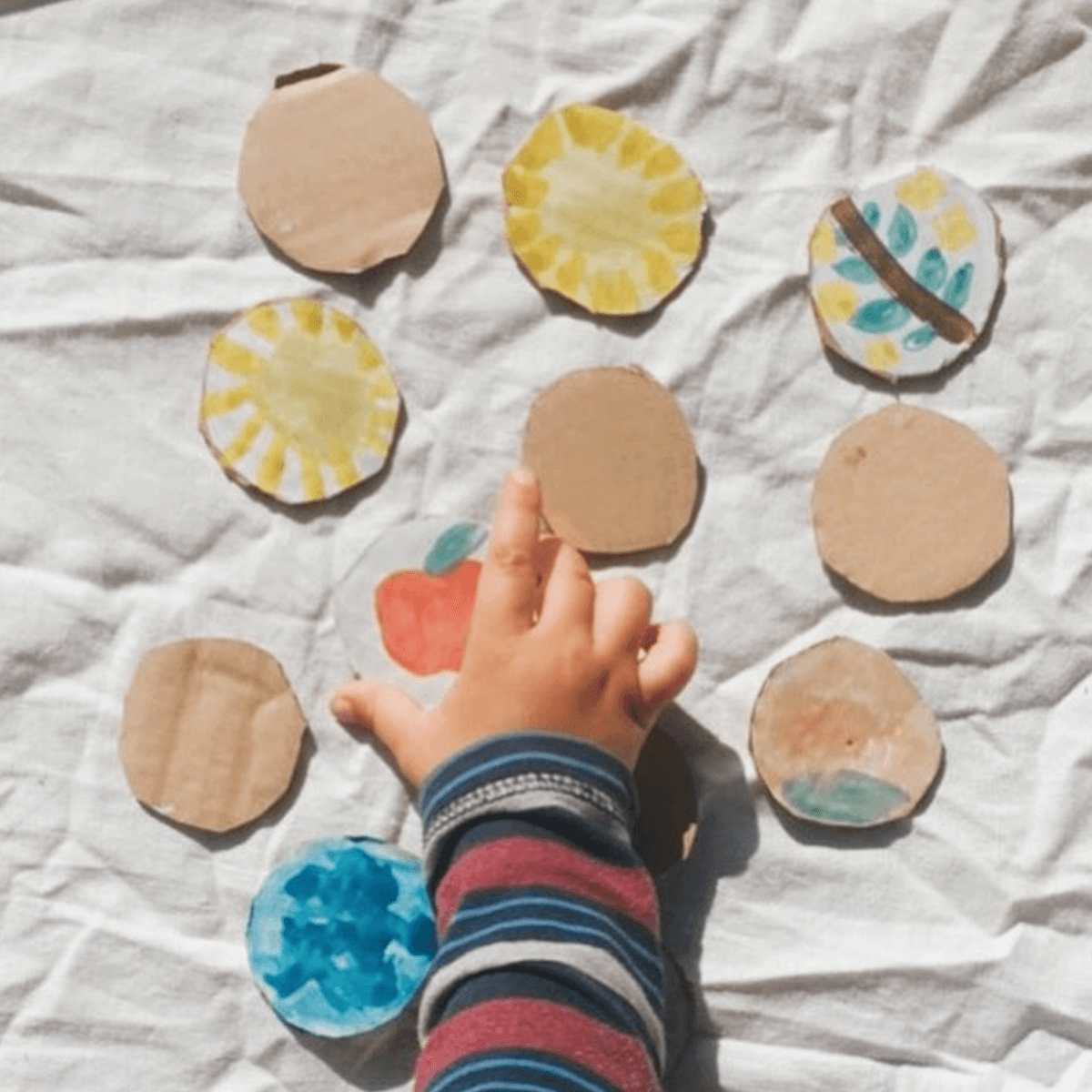 child reaching for a painted memory game created with cardboard and paint