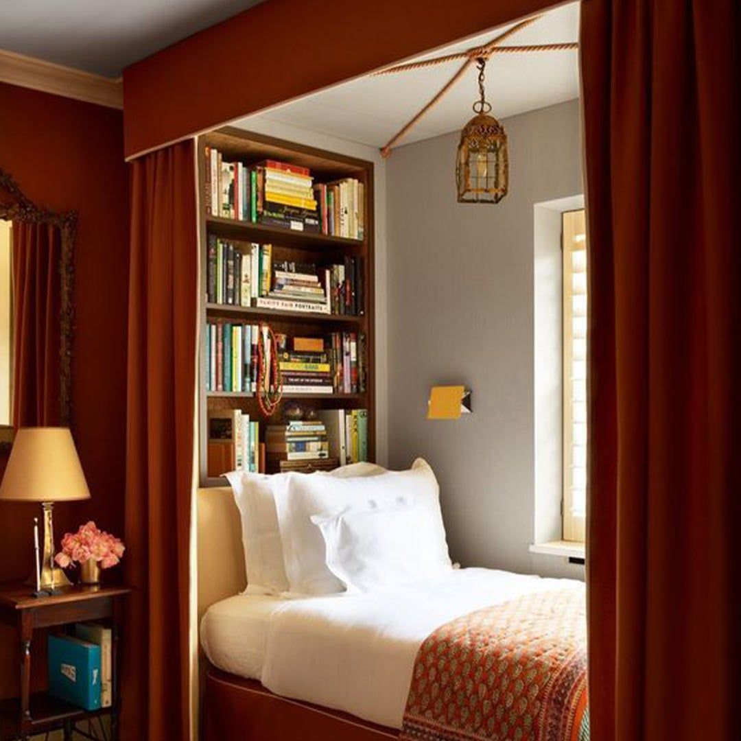 twin bed tucked away with a built in bookshelf and a dusty red canopy