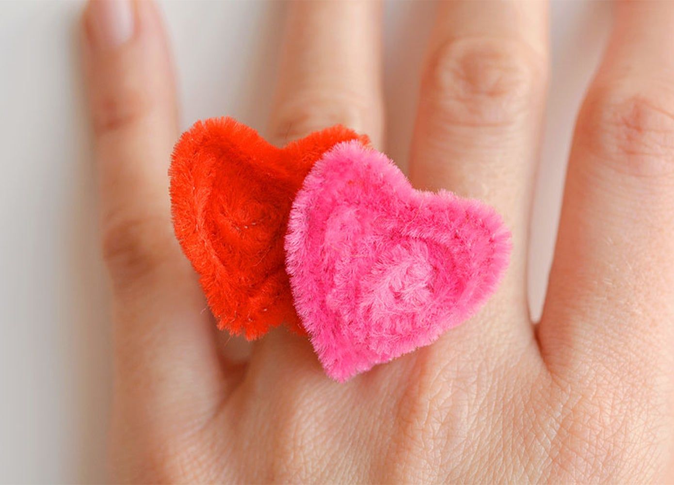 A ring in the shape of two hearts made of red and pink pipe cleaners