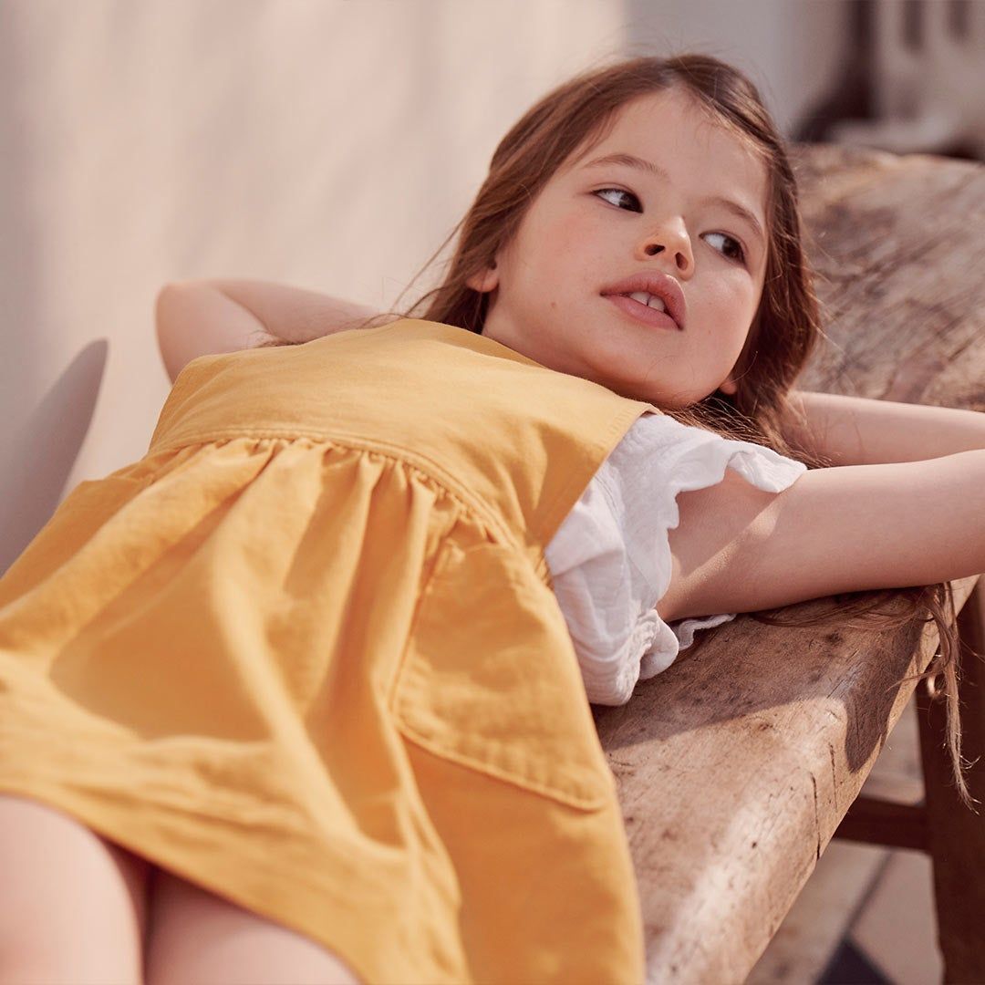 Girl in yellow dress laying on a bench