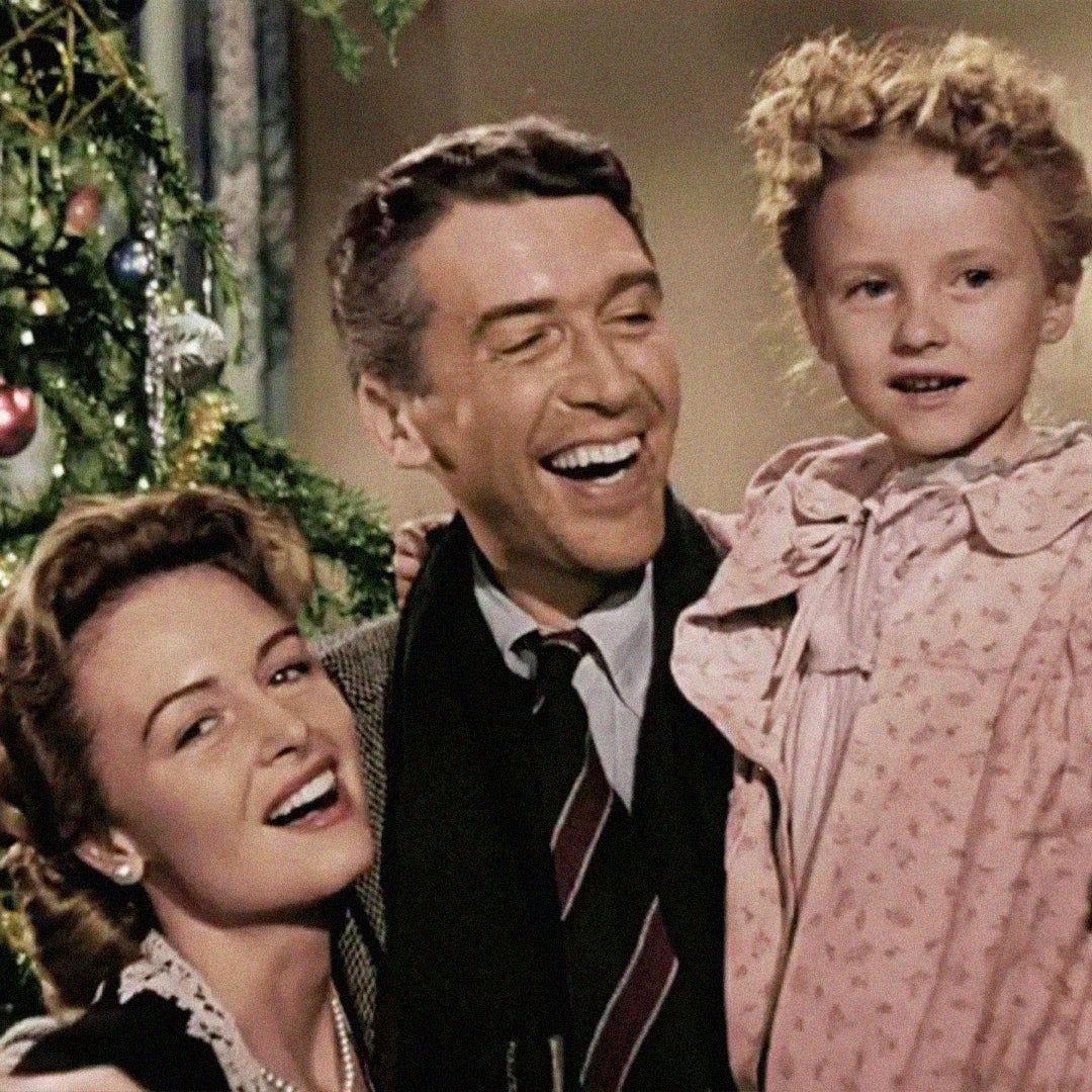 George, Mary, and Zuzu from It's A Wonderful Life smiling in front of a Christmas tree