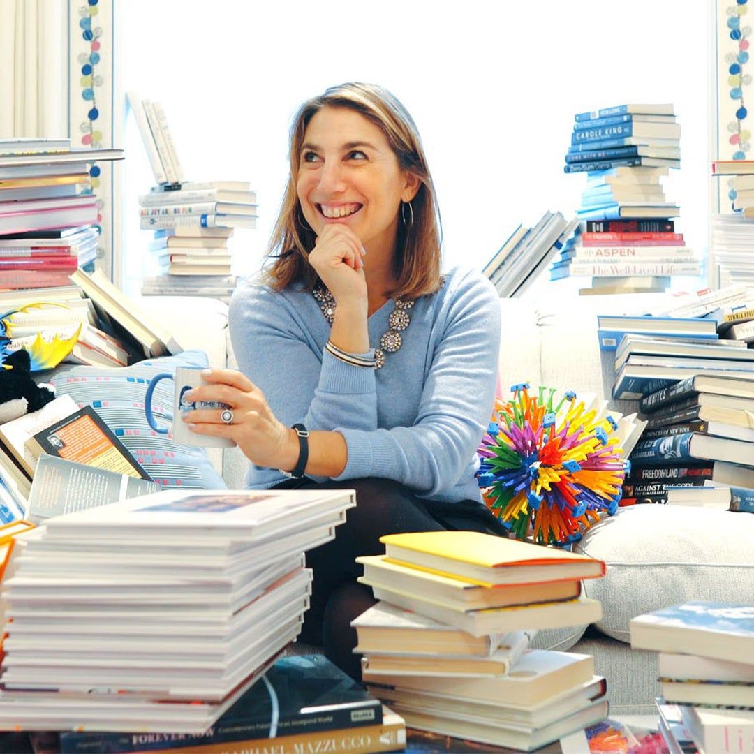 Author Zibby Owens sitting on a couch surrounded by stacks of books